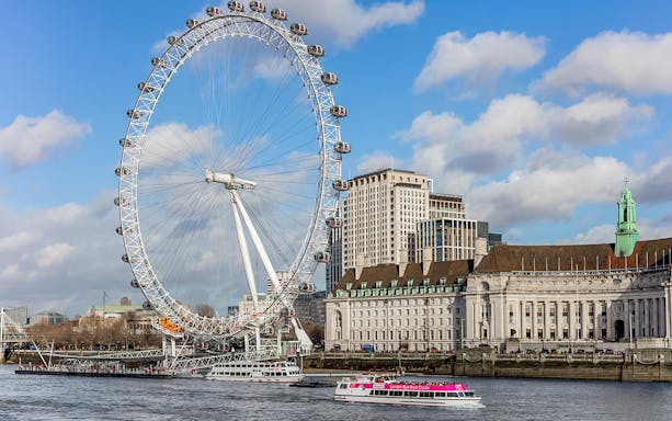 London Eye and river cruise boat on the Thames with cityscape in the background.