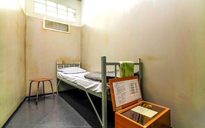 DDR Museum Berlin exhibit showing a recreated prison cell with a bed and documents.