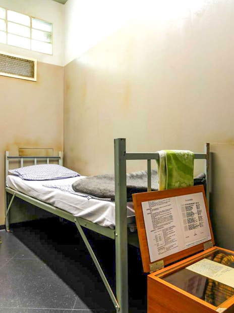 DDR Museum Berlin exhibit showing a recreated prison cell with a bed and documents.