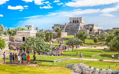 Iguana on Tulum ruins with tourists exploring ancient site in Mexico.