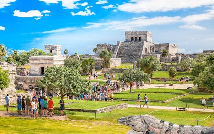 Iguana on Tulum ruins with tourists exploring ancient site in Mexico.