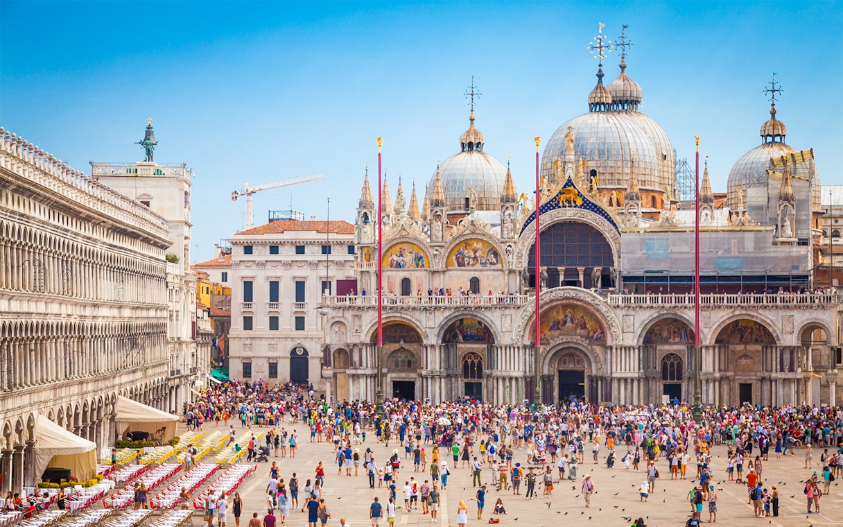 Crowd in front of St. Mark's Basilica, Venice, with ornate domes and arches.