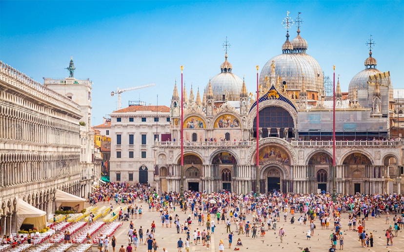 Crowd in front of St. Mark's Basilica, Venice, with ornate domes and arches.