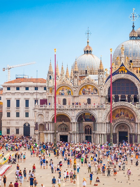 Crowd in front of St. Mark's Basilica, Venice, with ornate domes and arches.