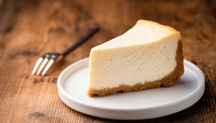 Cheesecake slice on a white plate with a fork beside it.