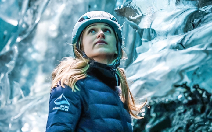 Person exploring inside a crystal ice cave wearing a helmet and winter jacket.