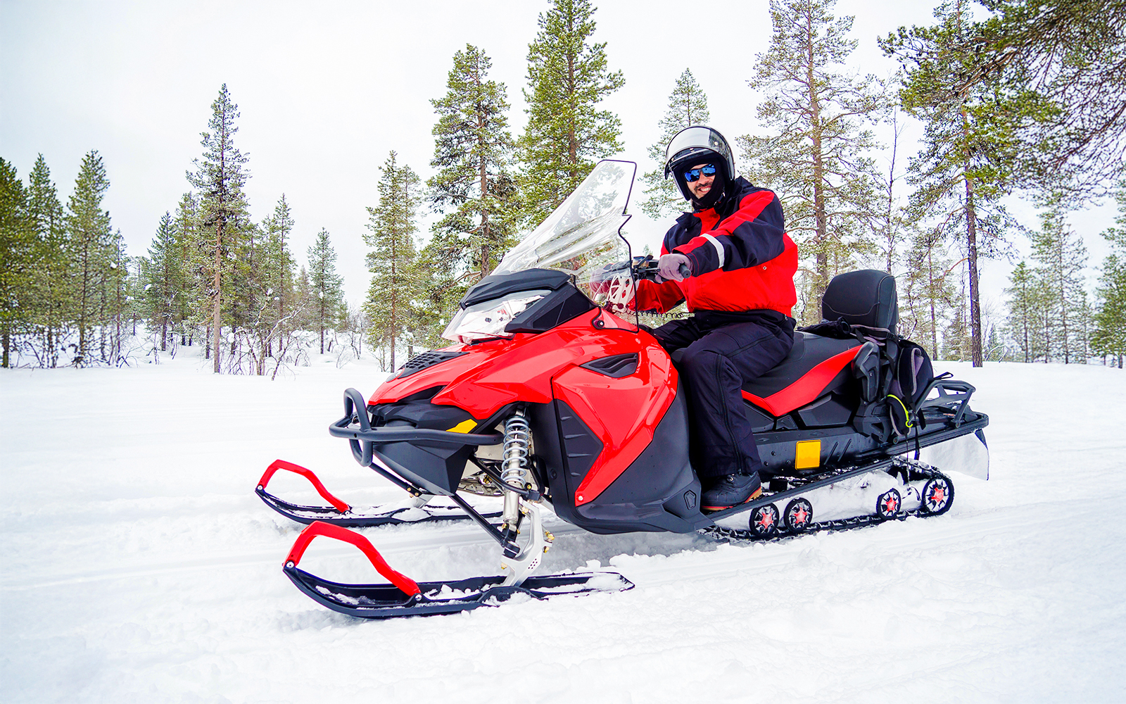 Man riding a snowmobile through snowy forest in Lapland.