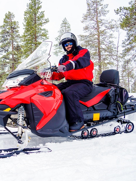 Man riding a snowmobile through snowy forest in Lapland.