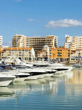 Yachts docked at Marina in Vilamoura, district Faro, Portugal with buildings in the background.