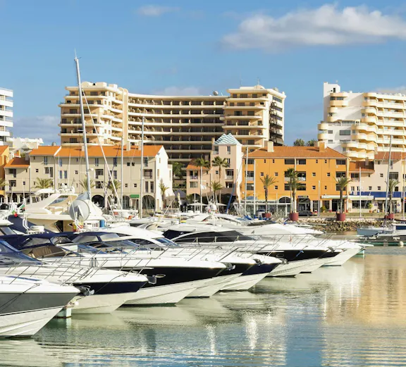 Yachts docked at Marina in Vilamoura, district Faro, Portugal with buildings in the background.