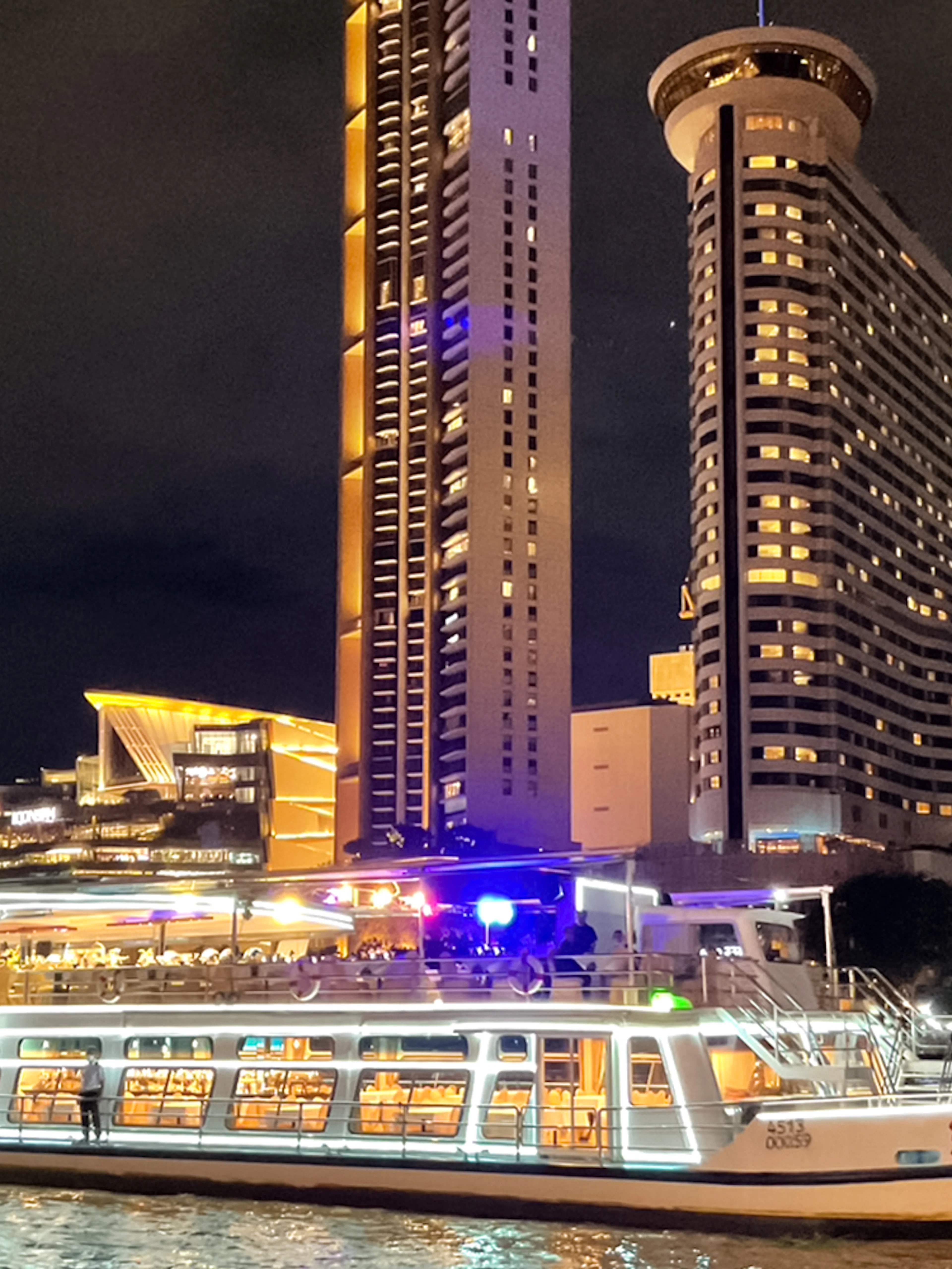 Chao Phraya cruise boat at night with Bangkok skyline in the background.