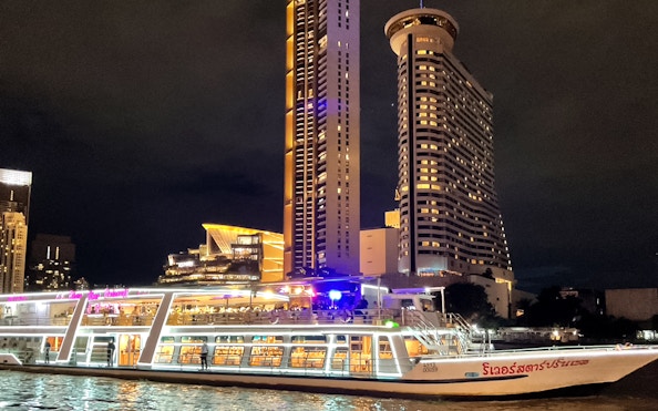 Chao Phraya cruise boat at night with Bangkok skyline in the background.