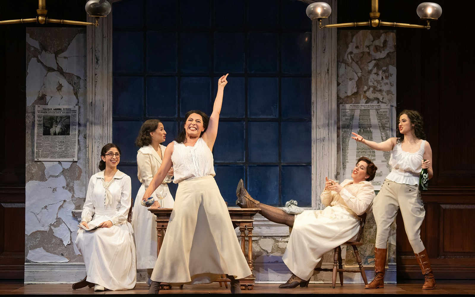 Women in period costumes performing a lively scene from the play "Suffs" on stage.