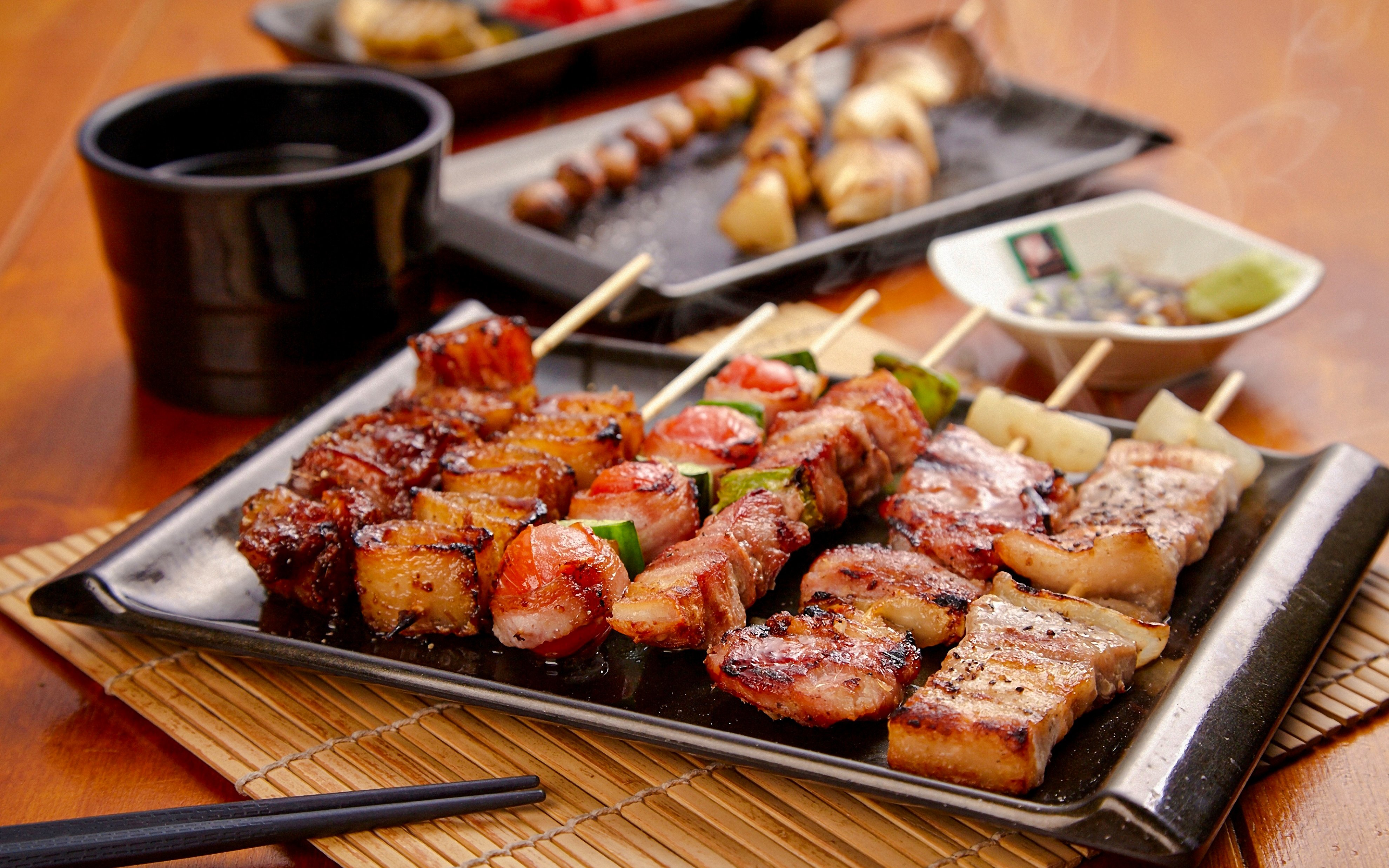 Grilled skewers on a plate in izakaya style with dipping sauce and chopsticks.
