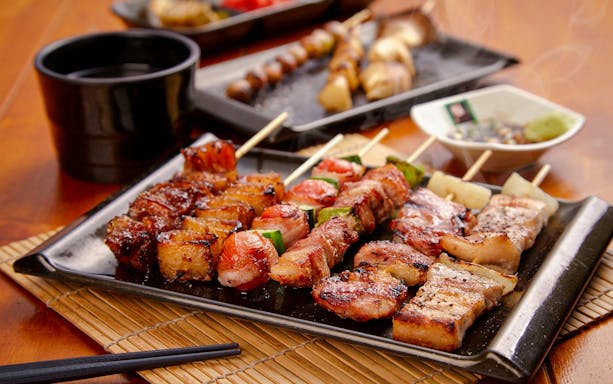 Grilled skewers on a plate in izakaya style with dipping sauce and chopsticks.
