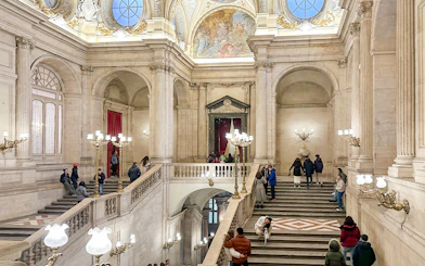 Main staircase of the Royal Palace of Madrid with visitors exploring the ornate architecture.