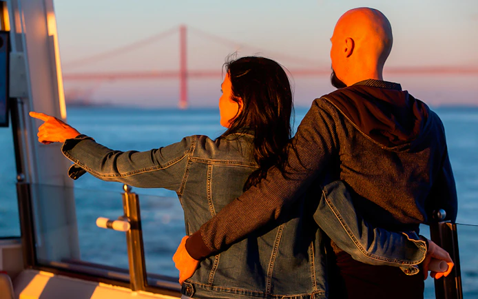 Couple enjoying sunset cruise on Tagus River, Lisbon with bridge view.