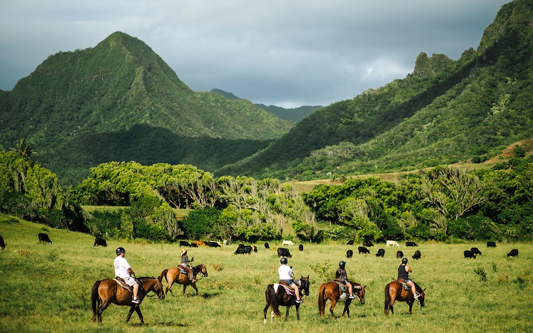 Horseback riders on a tour at Kualoa Ranch, Hawaii, with lush mountains in the background.