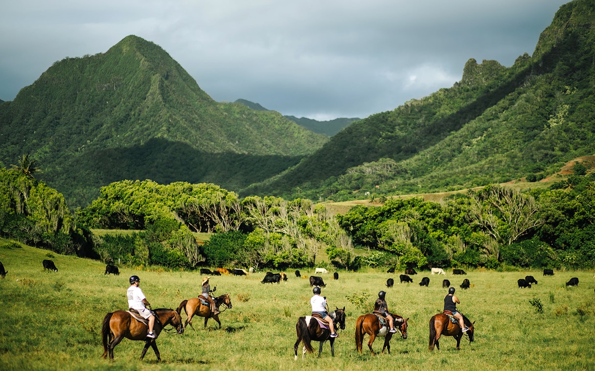 Horseback riders on a tour at Kualoa Ranch, Hawaii, with lush mountains in the background.
