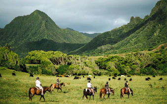 Horseback riders on a tour at Kualoa Ranch, Hawaii, with lush mountains in the background.