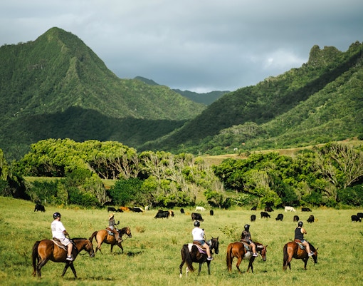 Horseback riders on a tour at Kualoa Ranch, Hawaii, with lush mountains in the background.