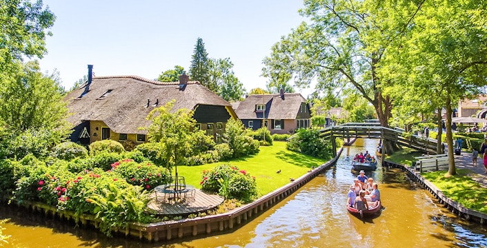 Giethoorn canal boat ride with traditional thatched-roof houses in the Netherlands.