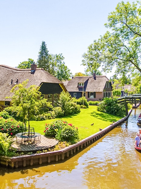 Boat ride through Giethoorn canal with thatched-roof houses and wooden bridge.