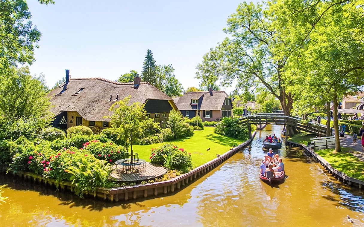 Boat ride through Giethoorn canal with thatched-roof houses and wooden bridge.