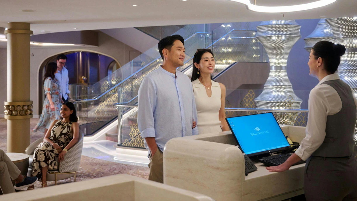 Couple at concierge lounge desk on luxury cruise ship with elegant decor.
