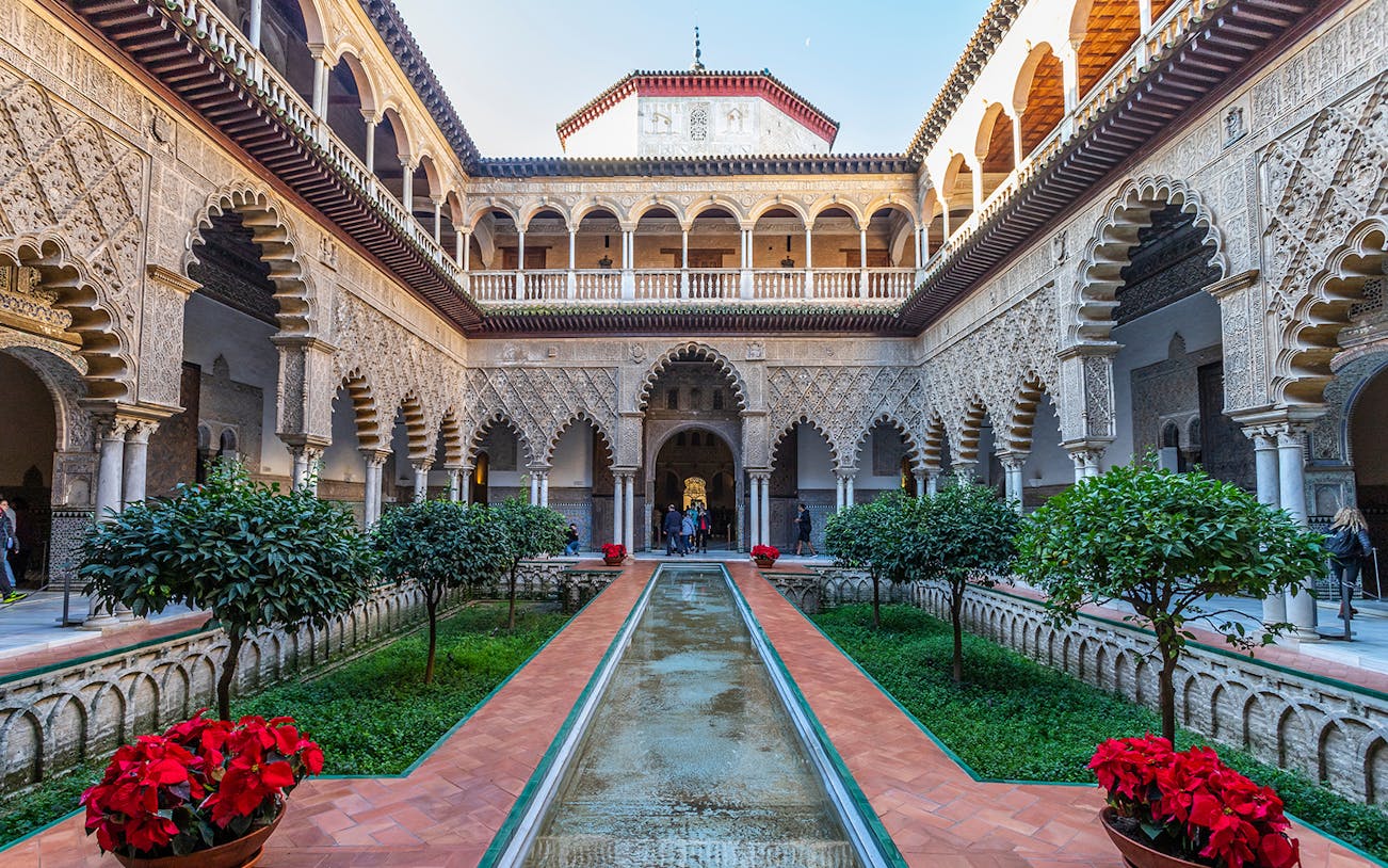 Alcazar Seville courtyard with intricate arches and lush gardens.
