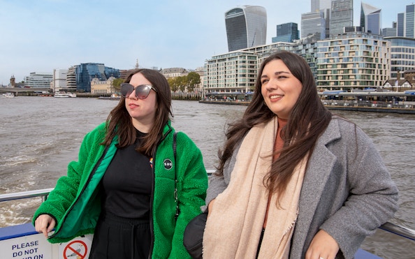 Women enjoying a Thames River afternoon cruise with London skyline in the background.
