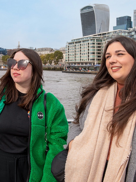 Women enjoying a Thames River afternoon cruise with London skyline in the background.