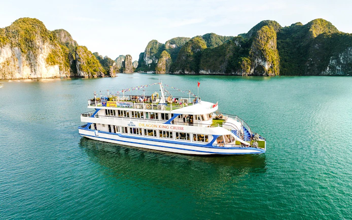 Delux Dragon King cruise ship sailing in Halong Bay, Vietnam, with limestone karsts in the background.