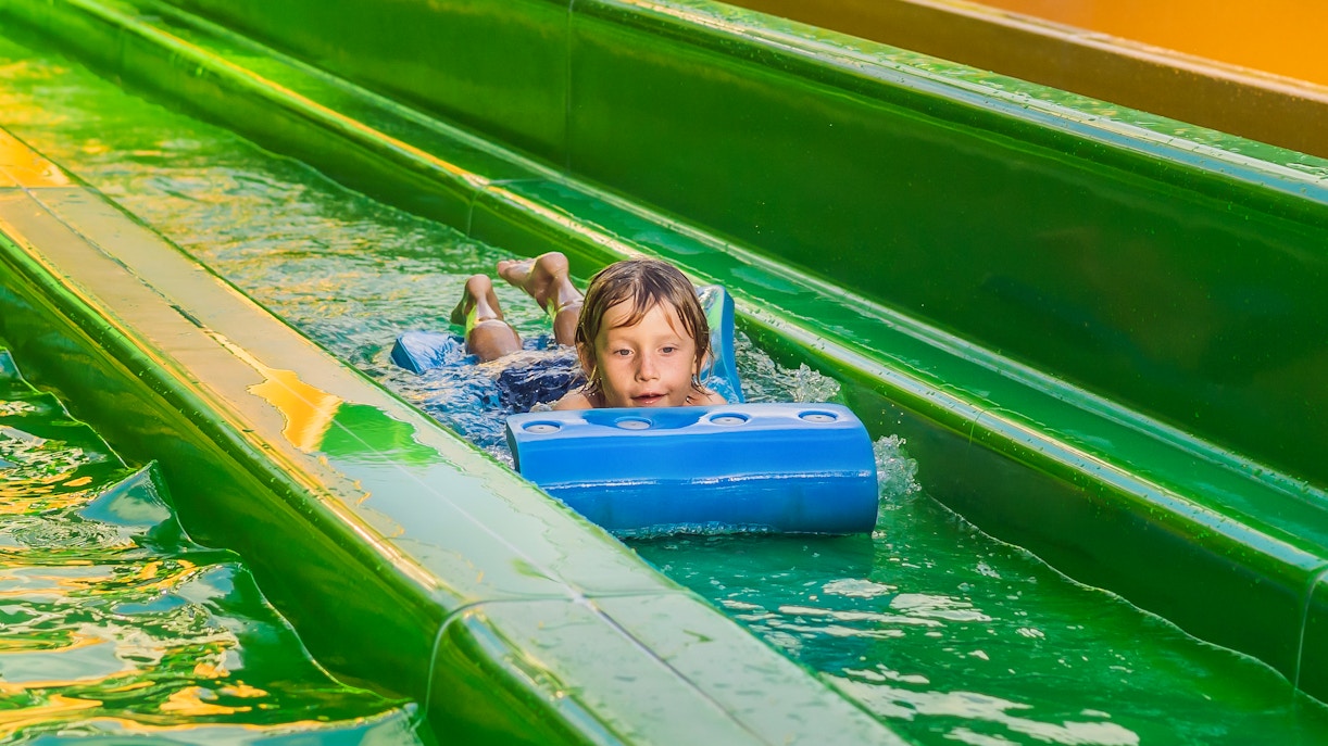 Boy sliding on a water slide at a tropical resort water park.