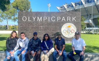 Group sitting at Melbourne Olympic Park sign during sports walking tour.