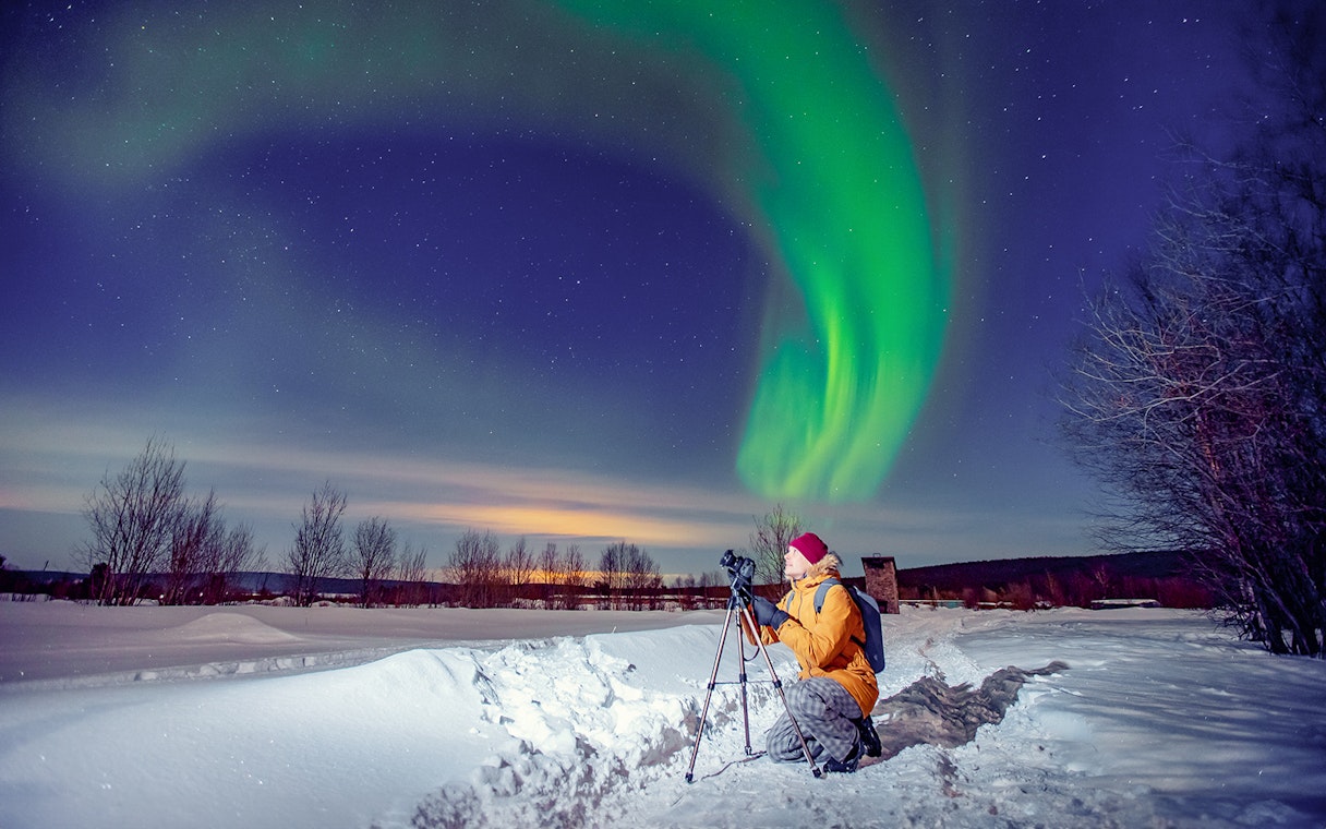 Person photographing Northern Lights on snowy landscape during Premium Small Group Northern Lights Tour.