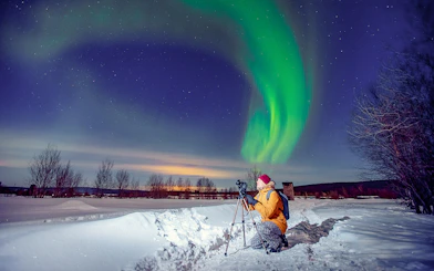 Person photographing Northern Lights on snowy landscape during Premium Small Group Northern Lights Tour.