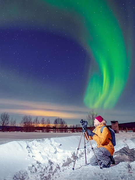 Person photographing Northern Lights on snowy landscape during Premium Small Group Northern Lights Tour.