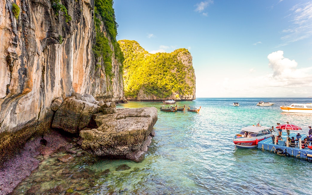 Boats docked at pier with limestone cliffs in Phi Phi Islands, Thailand.