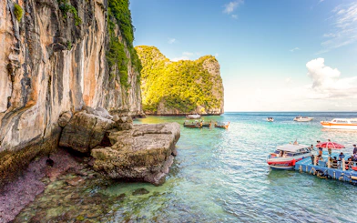 Boats docked at pier with limestone cliffs in Phi Phi Islands, Thailand.