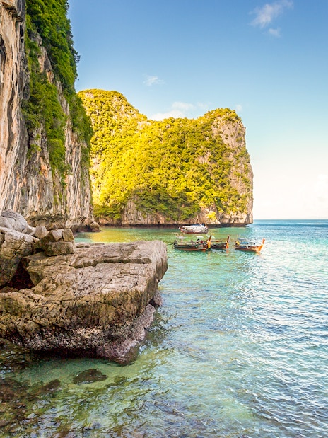 Boats docked at pier with limestone cliffs in Phi Phi Islands, Thailand.