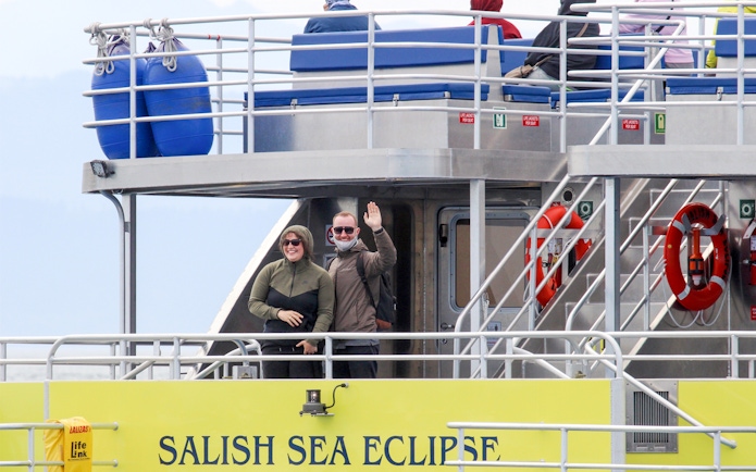 Guests waving on the Salish Sea Eclipse catamaran deck.
