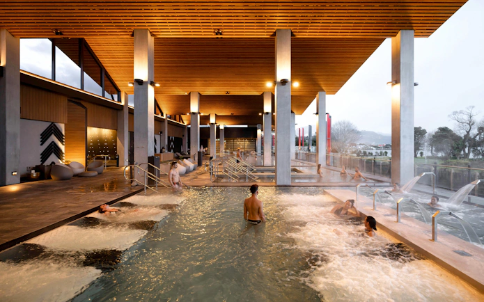 Guests enjoying hydropool at Wai Ariki Hot Springs & Spa, Rotorua, with lakeview and modern architecture.