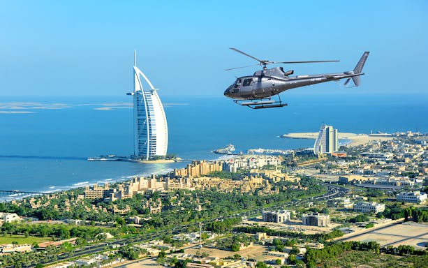 Helicopter flying over Dubai coastline with Burj Al Arab in view.
