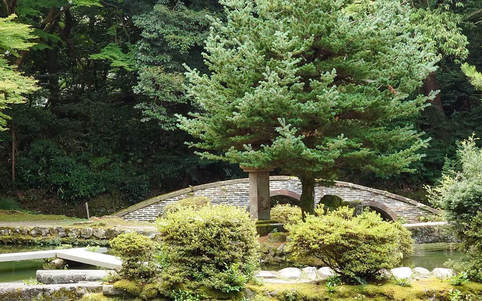 Stone bridge and lush greenery in a traditional Japanese garden in Kanazawa.