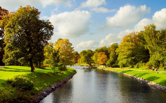 Boat on Djurgårdsbrunn Canal surrounded by autumn trees in Stockholm.