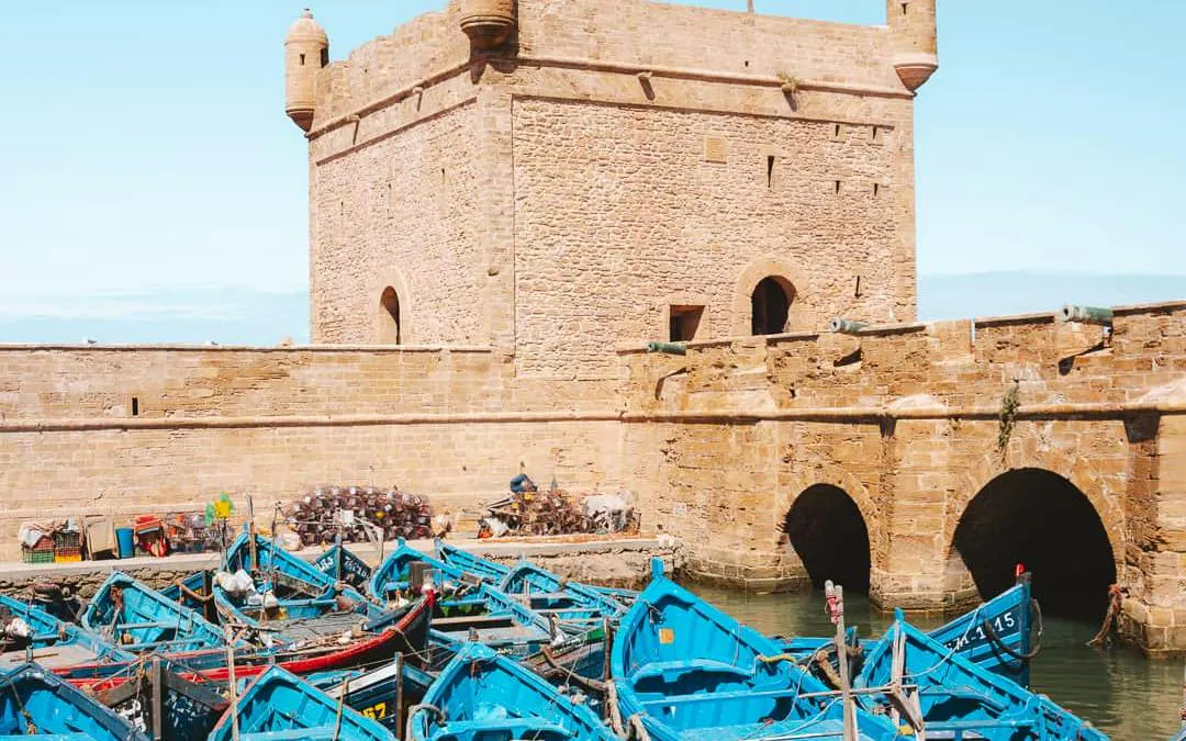 Blue fishing boats in the harbor of Essaouira with historic stone fortress walls.