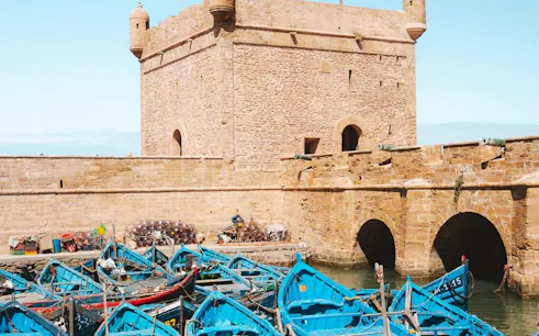 Blue fishing boats in the harbor of Essaouira with historic stone fortress walls.