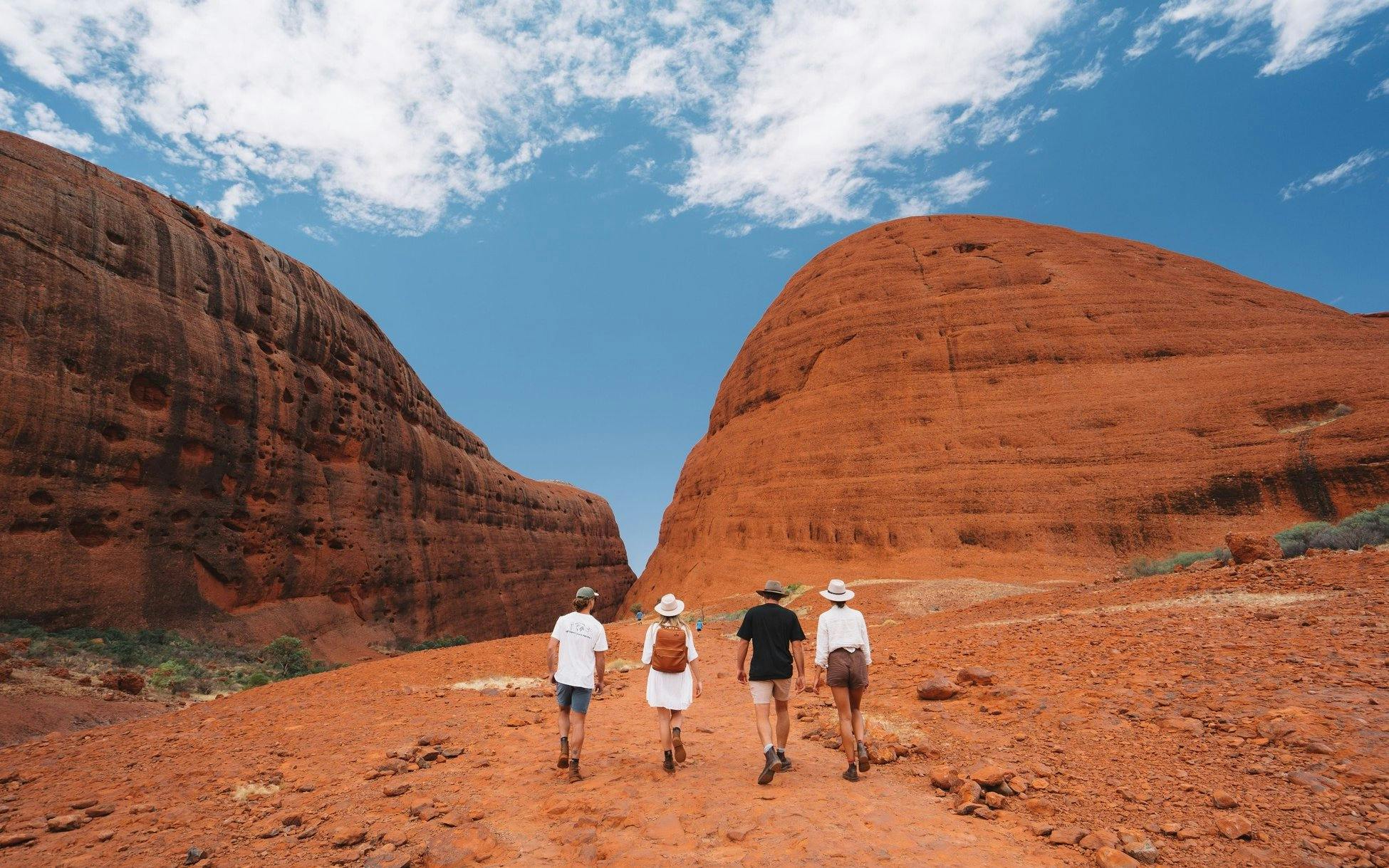 Group hiking between red rock formations at Kata Tjuta, Australia.