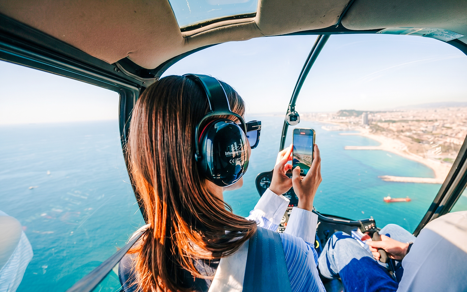 Helicopter passenger photographing coastal city view during shared panoramic tour.